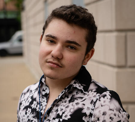 A cartoon drawing of Adrian, a white man with brown hair and blue headphones with a microphone.